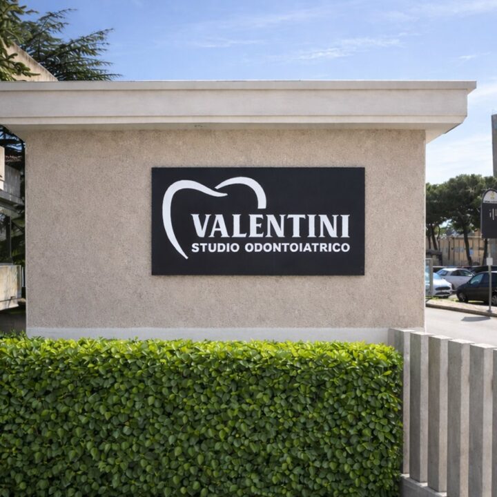 Insegna Valentini Studio Odontoiatrico sul muro d'ingresso con siepe