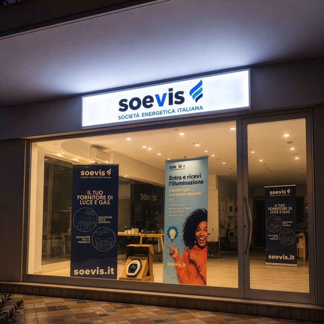 Insegna luminosa bianca Soevis Società Energetica Italiana sopra la vetrina del punto vendita, di sera
