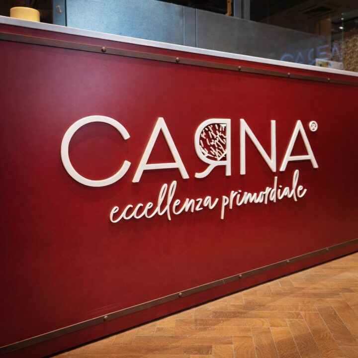 Scritta Carna eccellenza primordiale in plexiglas bianco in rilievo sul bancone rosso